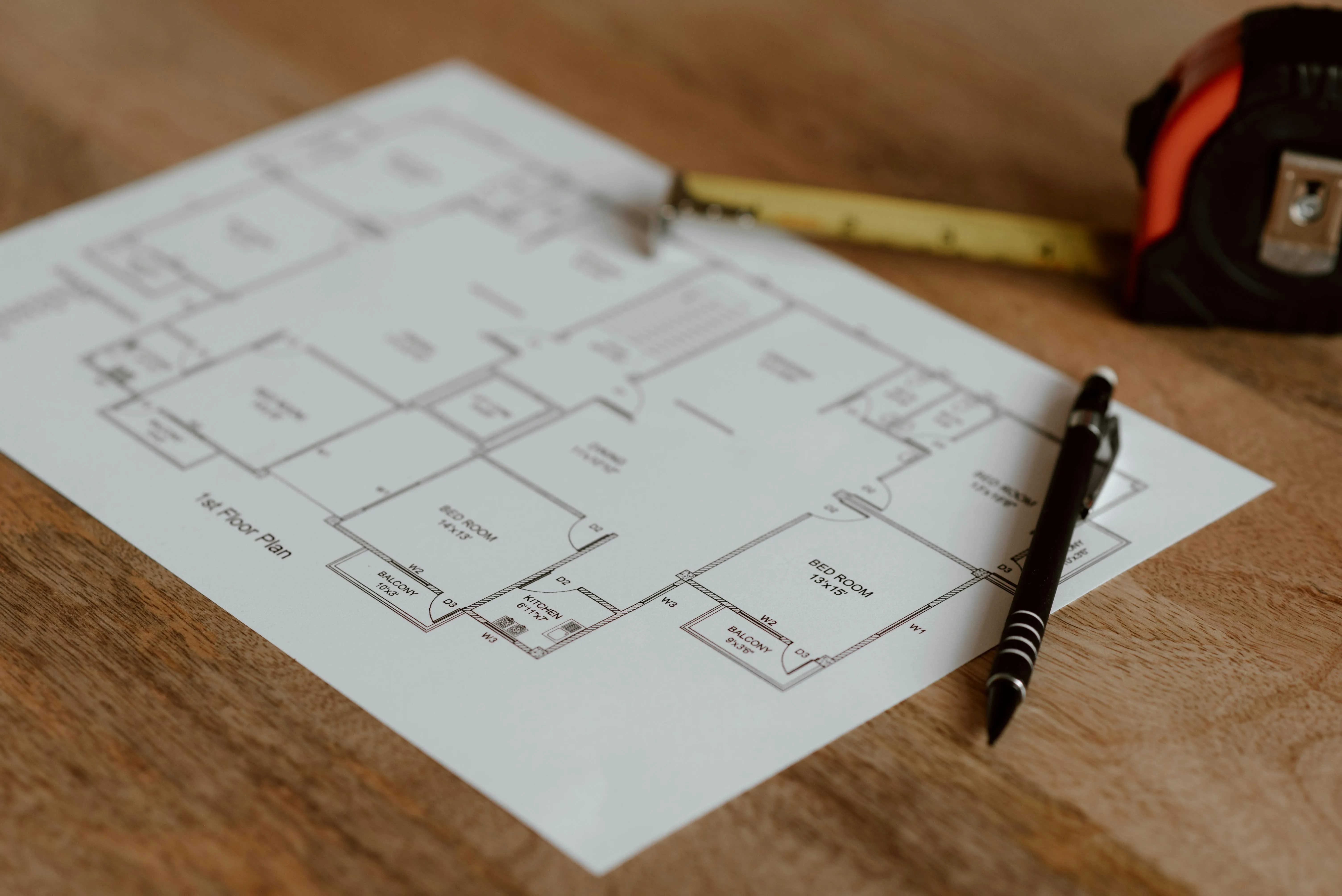 A blueprint of a house beside measuring tape and a pen