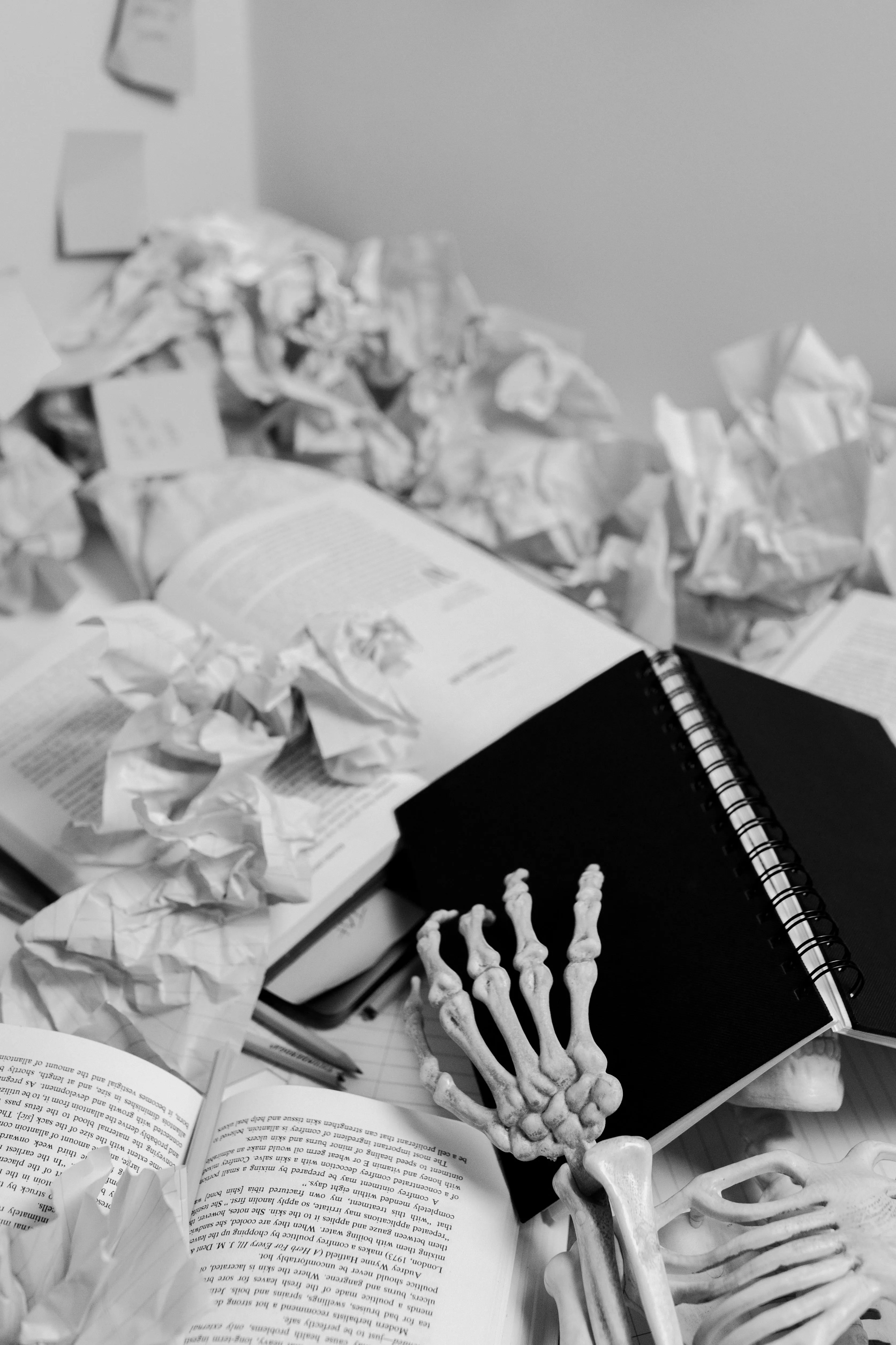A skeleton holds a notebook among crumpled paper balls